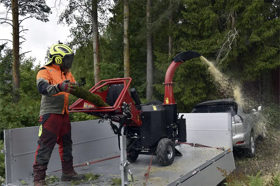 Työntekijä suojavarusteissa käyttää puutarhajätteen silppuria peräkärryn päällä